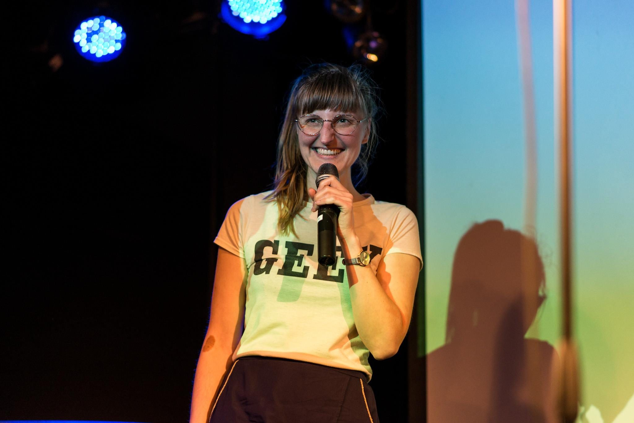 Adina Wilcke moderiert am Mikrofon im bunten Bühnenlicht (Foto: Helmut Prochart)